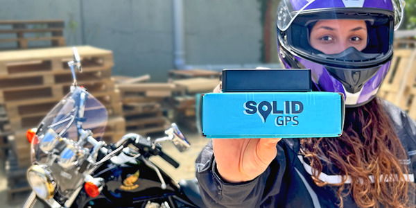 Solid GPS Tracker being held in front of a Motorcycle