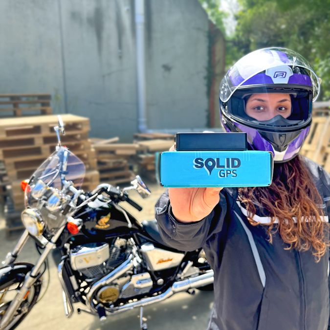 Solid GPS Tracker being held in front of a Motorcycle